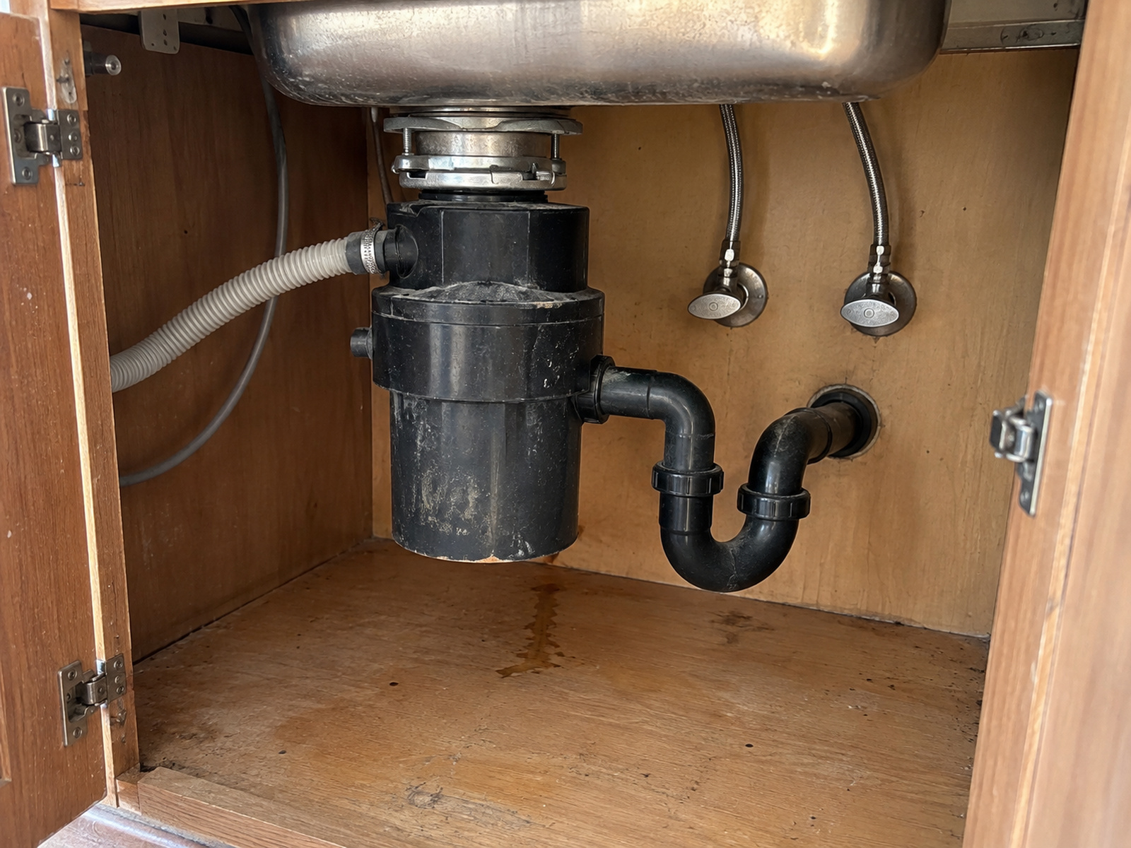 Garbage disposal and P-trap under a kitchen sink with the cabinet open