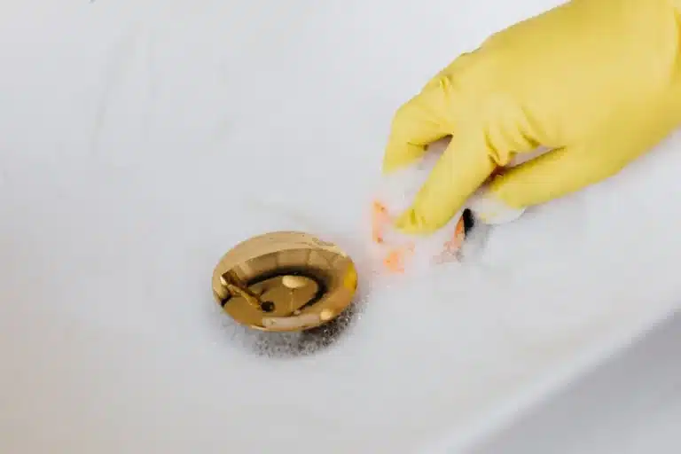 Gloved hand cleaning around a brass tub drain