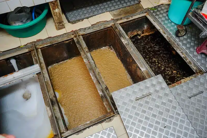 Open in-floor grease trap in a commercial kitchen with its covers removed