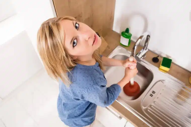 Woman using a plunger on a clogged kitchen sink