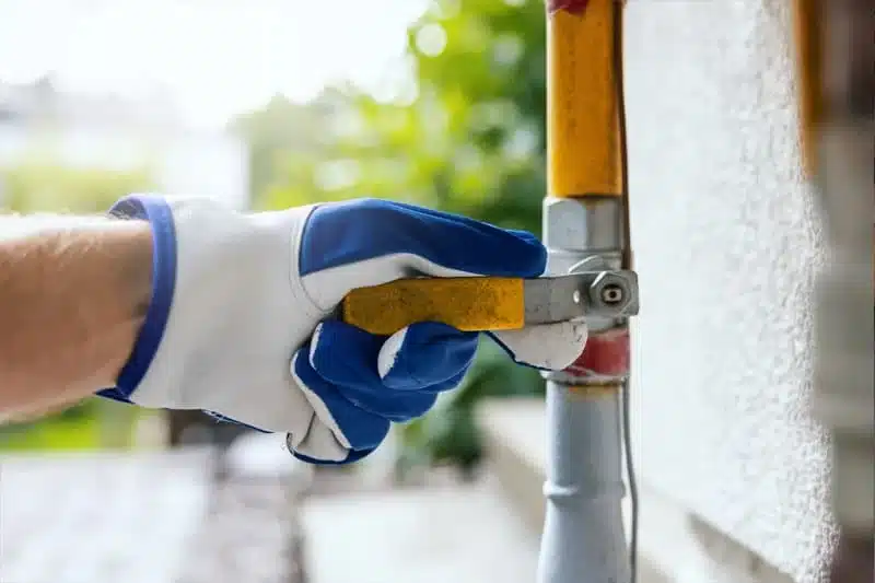 Gloved hand closing the shutoff valve on an outdoor gas line