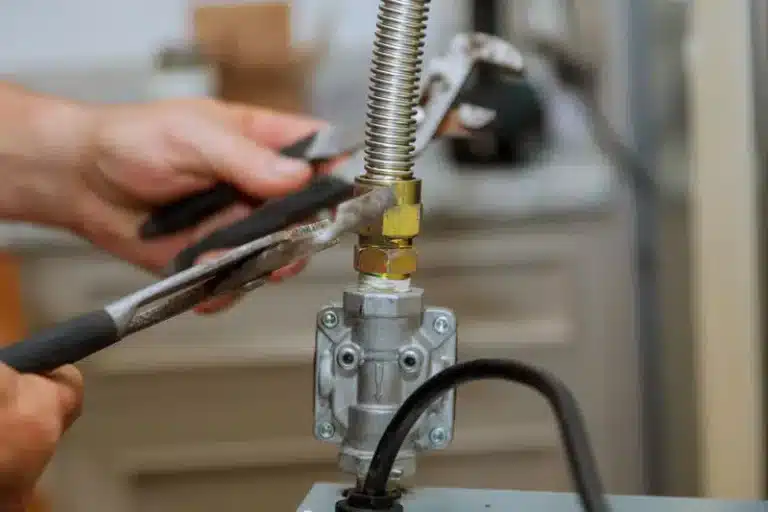 Hands tightening a flexible gas line fitting with two wrenches