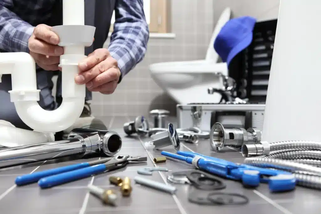 Plumber holding a white P-trap with tools laid out on a bathroom floor