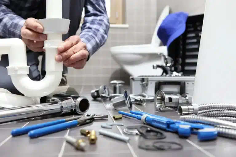 Plumber holding a white P-trap with tools laid out on a bathroom floor