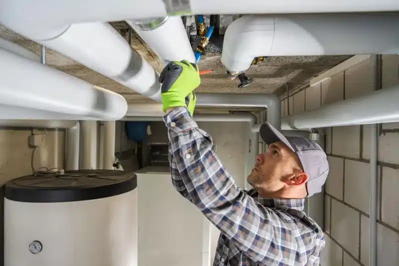 Plumber in a hard hat working on overhead pipes in a mechanical room